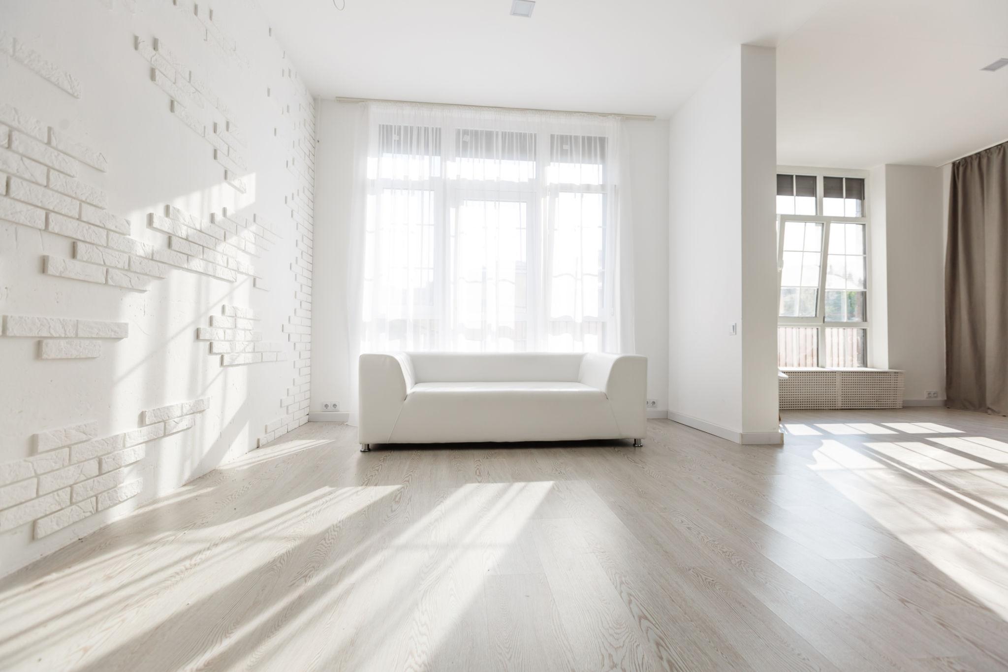 Bright living room with a white sofa, white brick wall, and light wood flooring.